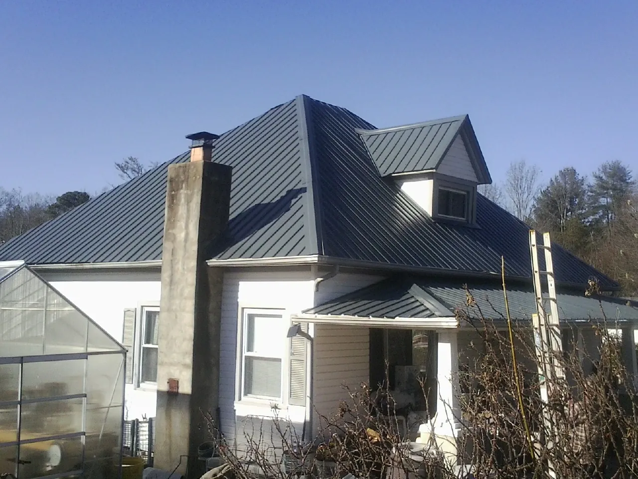 Dark blue standing seam metal roof on a white farmhouse with dormer — Slate & Tile Roof Repair by Roofing Brothers in East Hickory