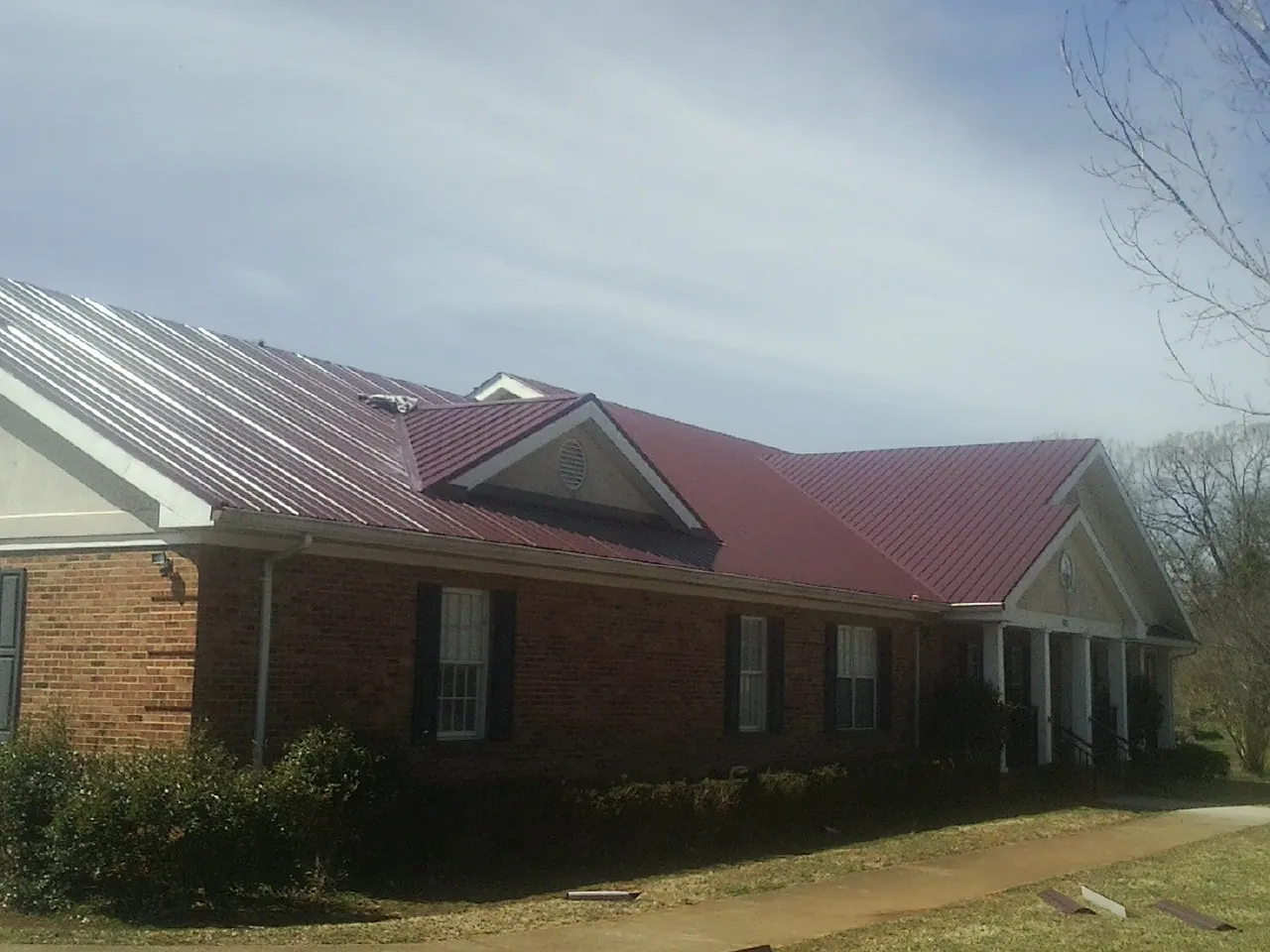 Red metal roof with gabled entries on a long brick building, from a Hail Damage Roof Repair job in East Hickory