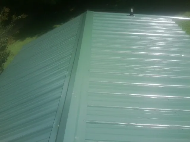 New green metal panels meeting at the ridge of a roof — Flat Roof Repair work by our crew in East Hickory