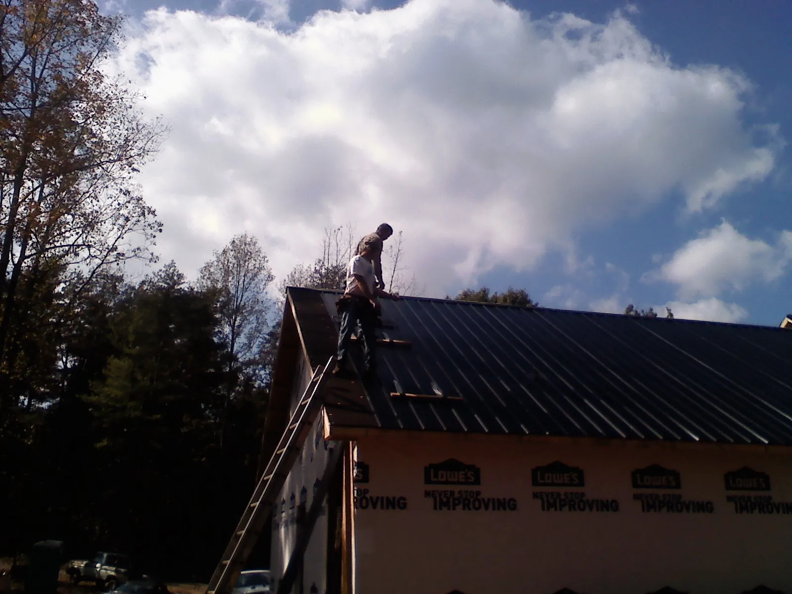 Roofer fastening dark metal panels high against a cloudy sky, from a Roof Inspection job in East Hickory