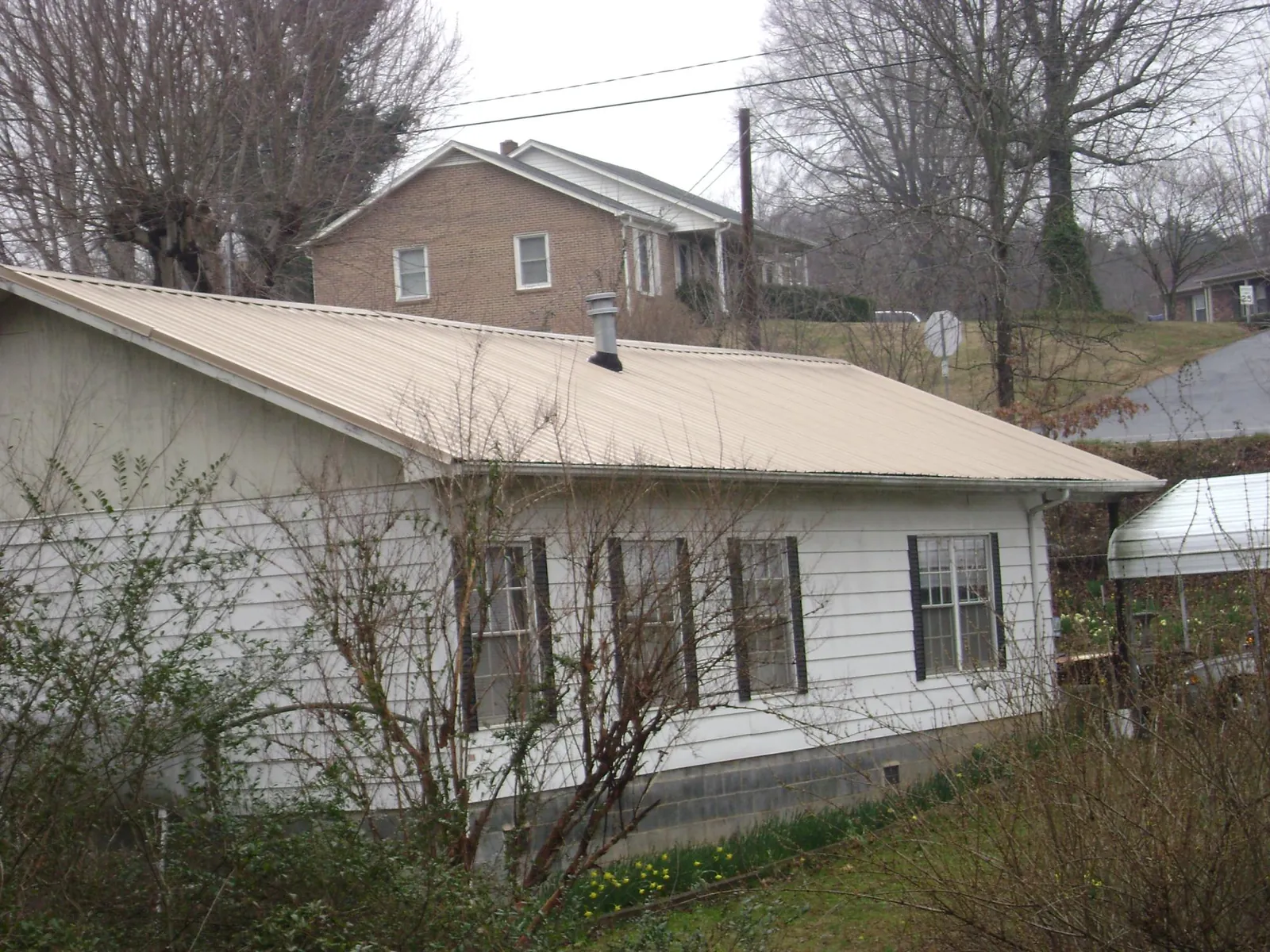 Tan metal roof on a white sided house set into a hillside — Commercial Roofing by Roofing Brothers in East Hickory
