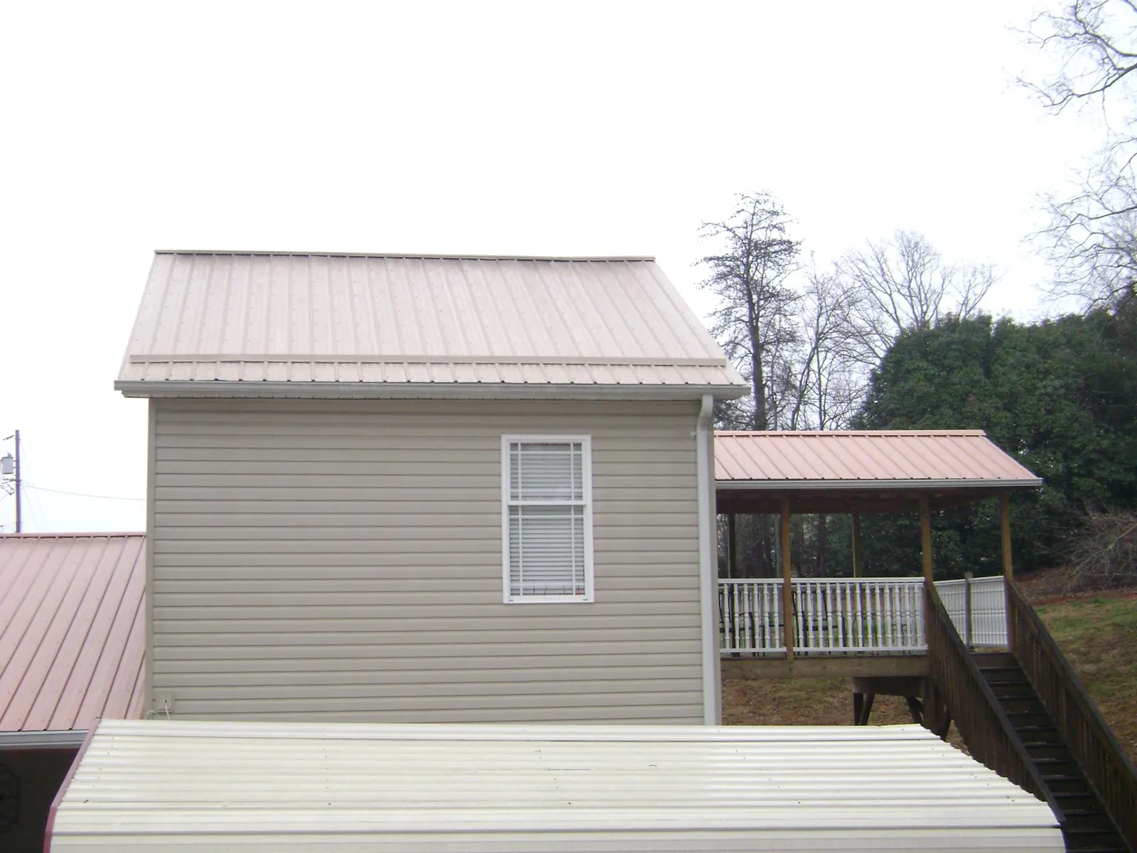 Tan metal roofs on a two story addition and attached porch, from a Roof Replacement job in East Hickory